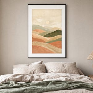 May include: A framed vertical wall art print featuring a watercolor landscape of rolling hills in shades of terracotta, sage green, and beige under a pale sun. The artwork is enclosed in a thin black frame and displayed on a neutral wall.