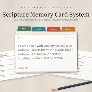 May include: A Scripture Memory Card System featuring 100 Bible verse cards in 12 topics with review tab dividers. The cards display text including John 14:27, How It Works instructions, and a list of topics. A pencil is placed at the bottom right.
