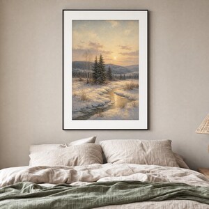 May include: A framed vertical wall art print depicting a winter landscape with a winding stream flowing through snow-covered ground, evergreen trees, and distant hills under a soft golden sunset sky with light clouds and a pale sun.