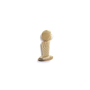 May include: A gold-toned metal lapel pin shaped like a basketball trophy. The design features a spherical basketball resting atop a conical net structure, all supported by a circular base. The surface has a polished, reflective finish.
