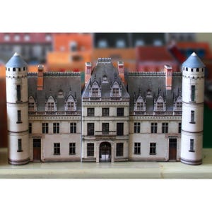 May include: A paper model of a white castle with grey roofs and many windows. The castle has two towers on either side and a central section with a large arched doorway.