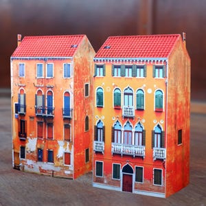 Può includere: Due edifici modello in miniatura con facciate arancioni e rosse. Gli edifici hanno più finestre e balconi. L'edificio a sinistra ha un aspetto consumato, mentre l'edificio a destra ha un aspetto più pulito.