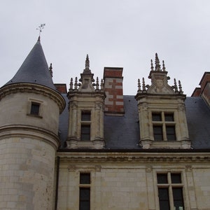 May include: A close-up view of a stone building with a pointed roof and multiple windows. The building has a gray slate roof and decorative stonework around the windows.