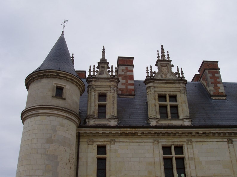 May include: A close-up view of a stone building with a pointed roof and multiple windows. The building has a gray slate roof and decorative stonework around the windows.