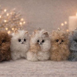 May include: Five fluffy, handmade kitten keyrings in varying colours: brown, white, tan, light brown, and grey. Each has a small silver loop for attaching to keys or a bag. The keyrings are displayed on a soft, textured surface.