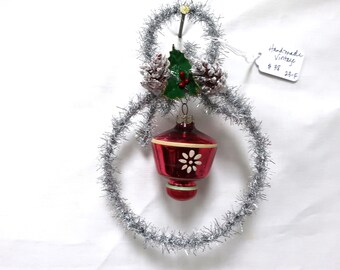 May include: Vintage Christmas ornament with a red glass bulb, white floral design, and silver tinsel. The ornament is decorated with pinecones and a green leaf. A tag reads "Handmade Vintage".
