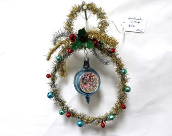 May include: A vintage Christmas ornament wreath made of gold and silver tinsel with red and blue bells. The wreath is decorated with a blue glass ornament with a pink and white design. The wreath is 25 inches in diameter. Handmade Vintage.