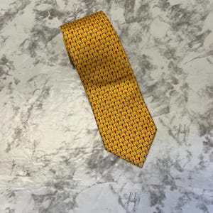 May include: A yellow tie with a repeating pattern of cocktail glasses in red, black, and yellow. The tie is made of a smooth fabric and is folded over itself.