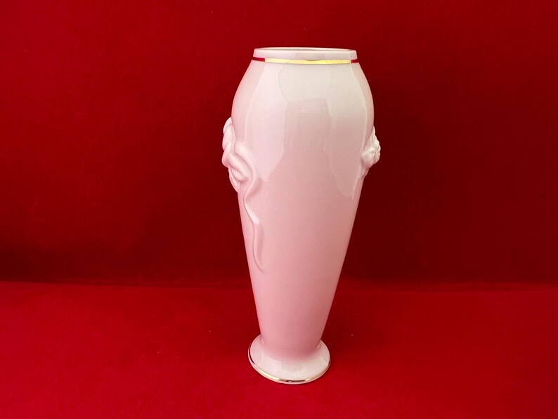 May include: A white porcelain vase with a gold rim and floral detailing. The vase has a slender, elegant shape.