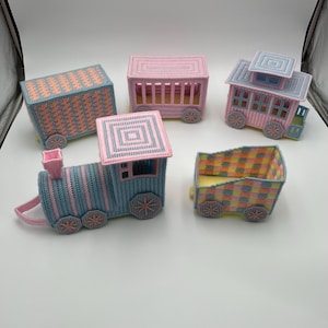 May include: A collection of colorful, handcrafted plastic canvas train cars. The train cars are in shades of pink, blue, and yellow, with intricate woven patterns. Each car has decorative wheels, and the train engine has a chimney.