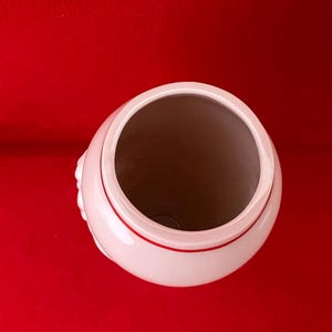 May include: A white ceramic vase with a red rim. The vase has a smooth, rounded shape and a wide opening.