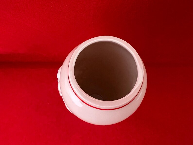 May include: A white ceramic vase with a red rim. The vase has a smooth, rounded shape and a wide opening.