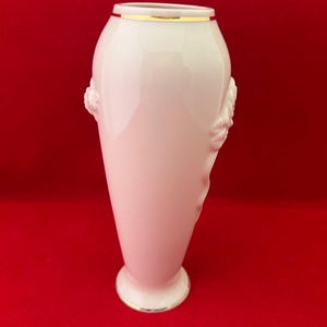May include: A white porcelain vase with a gold rim and floral detailing. The vase is tall and slender with a rounded base.