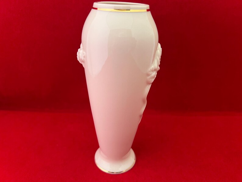 May include: A white porcelain vase with a gold rim and floral detailing. The vase is tall and slender with a rounded base.