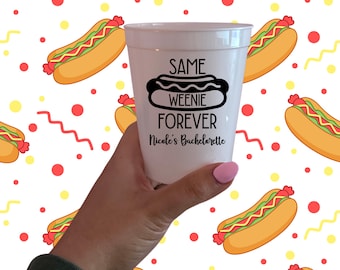 Può includere: Un bicchiere di plastica bianco con la scritta "SAME WEENIE FOREVER Nicole's Bachelorette" in nero. Il bicchiere è tenuto in mano con lo smalto rosa. Lo sfondo presenta un motivo di hot dog, punti rossi e zig-zag gialli.