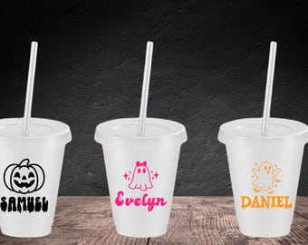 Può includere: Tre bicchieri di plastica bianca con coperchi e cannucce. Il primo bicchiere presenta una grafica di zucca nera e il nome SAMUEL. Il secondo bicchiere ha una grafica di fantasma rosa con un fiocco e il nome Evelyn. Il terzo bicchiere mostra un fantasma arancione e DANIEL.