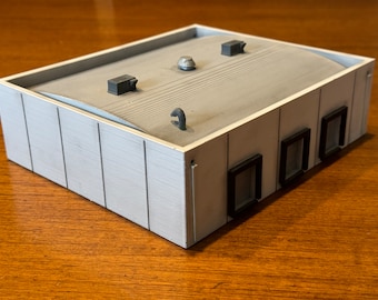 May include: A white model building with a gray roof and four black windows. The roof has a slight curve and several small details, including a vent pipe and a small dome.