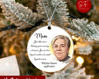 May include: A white round ornament with a picture of a woman and the text "Mom Your life was a blessing your memory a treasure You are love beyond words and missed beyond measure Wilma Snow 1938-2007".