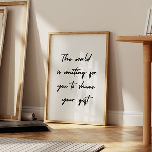 May include: A framed inspirational quote print with a white background and black text that reads "The world is waiting for you to shine your gift".