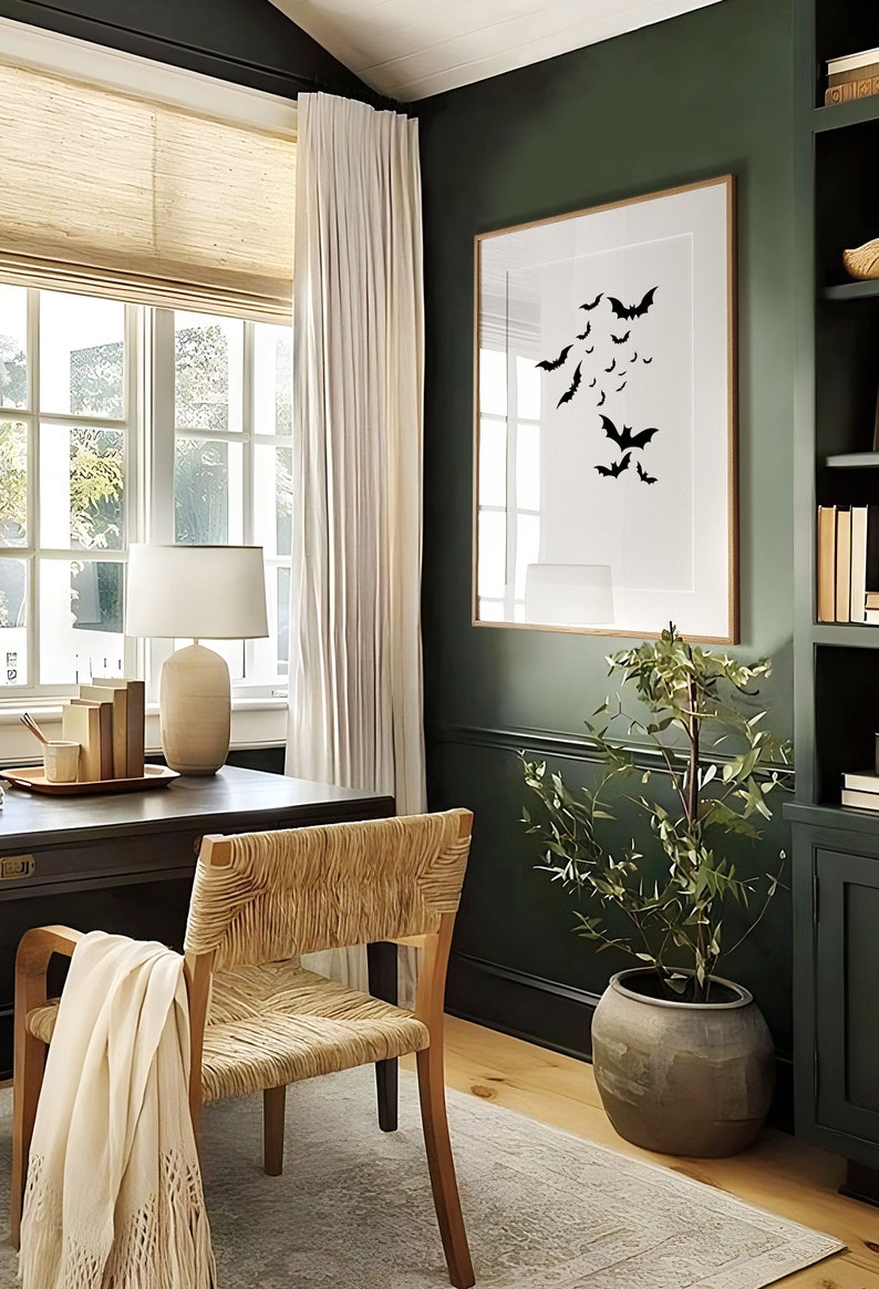 May include: A dark green home office with a wooden desk, a woven chair, a white lamp, and a framed print of black bats on a white background. A potted plant sits in the corner of the room.