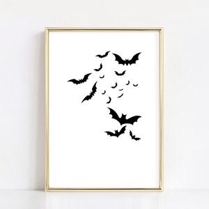 May include: A black and white printable wall art print featuring a silhouette of bats flying in a cluster. The print is framed in a gold frame.