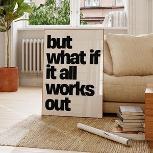 以下が含まれることがあります： 「but what if it all works out」の文字が黒字で書かれたフレーム入りのポスター。ベージュのソファ、織りのラグ、鉢植えの植物がある部屋にポスターが飾られています。部屋には自然光が入る窓があります。