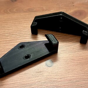 Op de afbeelding: Twee zwarte, 3D-geprinte beugels van plastic met gaten voor montage.