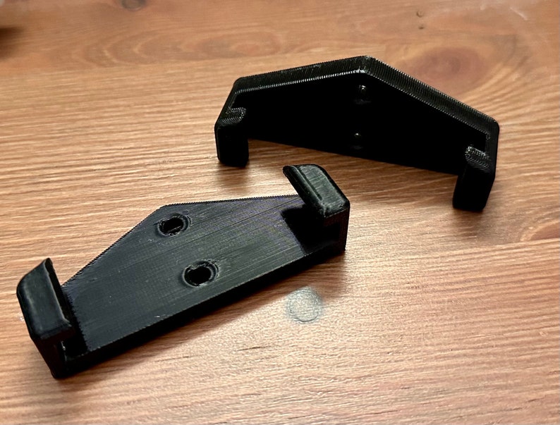 Op de afbeelding: Twee zwarte, 3D-geprinte beugels van plastic met gaten voor montage.