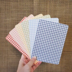 May include: A hand holds a fan of rectangular cards with rounded corners. Each card features a different color of gingham pattern, including red, pink, yellow, green, light blue, and navy blue. The cards are arranged in a fanned-out display.