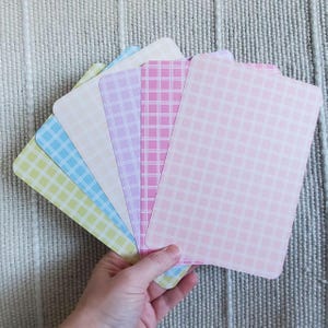 May include: A collection of pastel-colored cards with a grid pattern. The cards are in shades of pink, purple, blue, and yellow. The cards have rounded corners and are fanned out, showcasing the variety of colors and designs.
