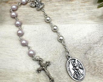 May include: A white and pink beaded rosary with a silver angel charm, a silver cross, and a silver pendant with the words "Guardian Angel" and an image of an angel.