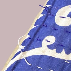May include: A close-up of a blue and white fabric with a white pattern. The fabric is sewn together with purple thread.