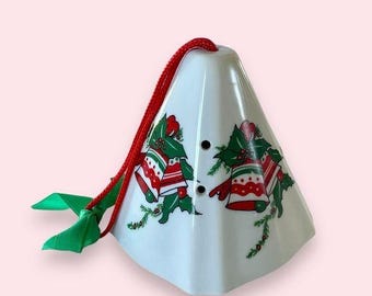 May include: White ceramic Christmas tree ornament shaped like a cone with a red ribbon and green holly leaves with red bells.