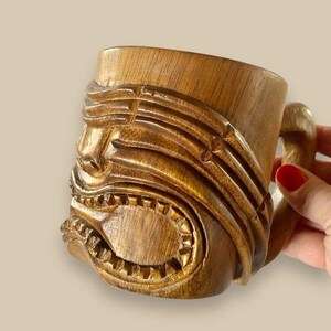 May include: A wooden tiki mug with a carved face and a handle. The mug is brown and has a glossy finish.