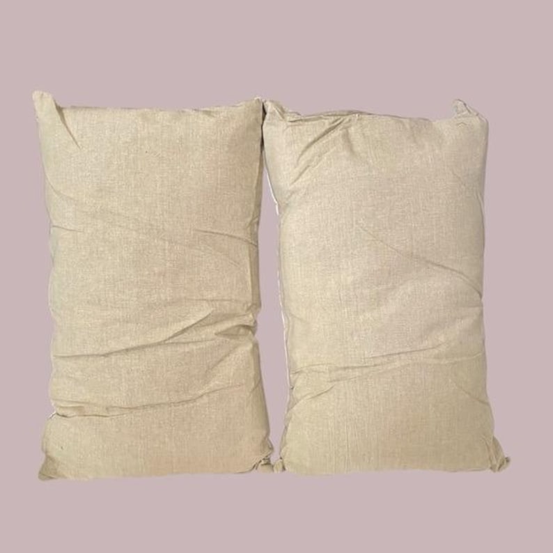 May include: Two beige pillowcases made of a soft, textured fabric. The pillowcases are lying flat on a light purple background.