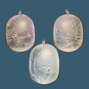 May include: Set of three oval wall plaques featuring pastoral scenes. Each plaque depicts children near a wooden fence, with soft, muted colors and a vintage aesthetic. The plaques have a dark border and a small loop for hanging.