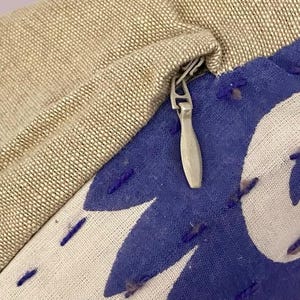 May include: A close-up of a zipper on a beige and blue pillow cover. The zipper is silver and has a pull tab. The pillow cover has a blue floral design.