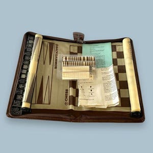 May include: A brown leather travel case with a chessboard and backgammon board inside. The case has a zipper closure and includes playing pieces and instructions.