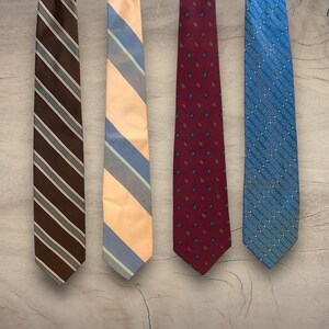 May include: Four different patterned neckties hanging on a light wood background. The ties are brown and white striped, light peach and blue striped, burgundy with a small floral pattern, and blue with a white and green geometric pattern.