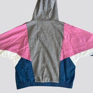 May include: A gray hooded sweatshirt with pink, white, and blue color-blocked panels. The sweatshirt has a drawstring hood and a ribbed hem.