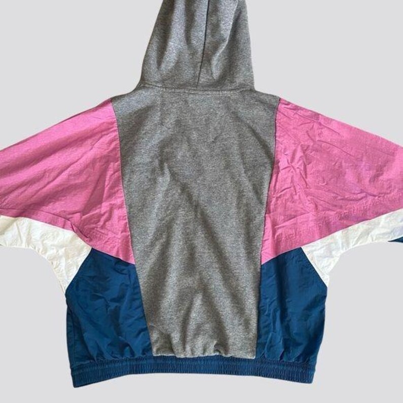 May include: A gray hooded sweatshirt with pink, white, and blue color-blocked panels. The sweatshirt has a drawstring hood and a ribbed hem.