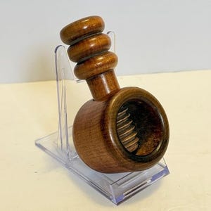 May include: A wooden nutcracker with a dark brown finish. The nutcracker has a round body with a threaded interior and a handle with three stacked, rounded sections. It is displayed on a clear plastic stand.