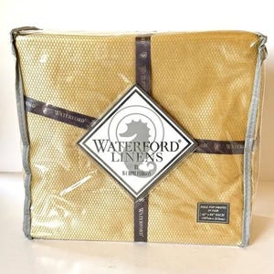May include: A package of Waterford Linens pole top drapes in a golden yellow color. The package is sealed in clear plastic and features the Waterford Linens logo and product information. The drapes measure 42" x 84" each.