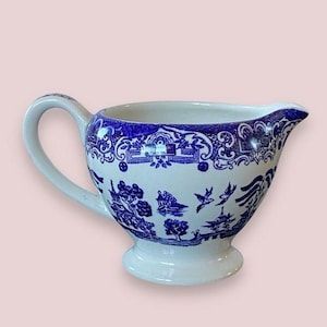 May include: A blue and white porcelain creamer with a traditional Chinese design. The creamer has a wide, rounded base and a spout on one side.
