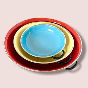 May include: A set of three colorful serving bowls. The largest bowl is red, the middle bowl is yellow, and the smallest bowl is blue. The bowls have a silver trim and are stacked together.