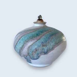 May include: A white ceramic vase with a round body and a lid. The vase has a blue and purple glaze with a textured finish.