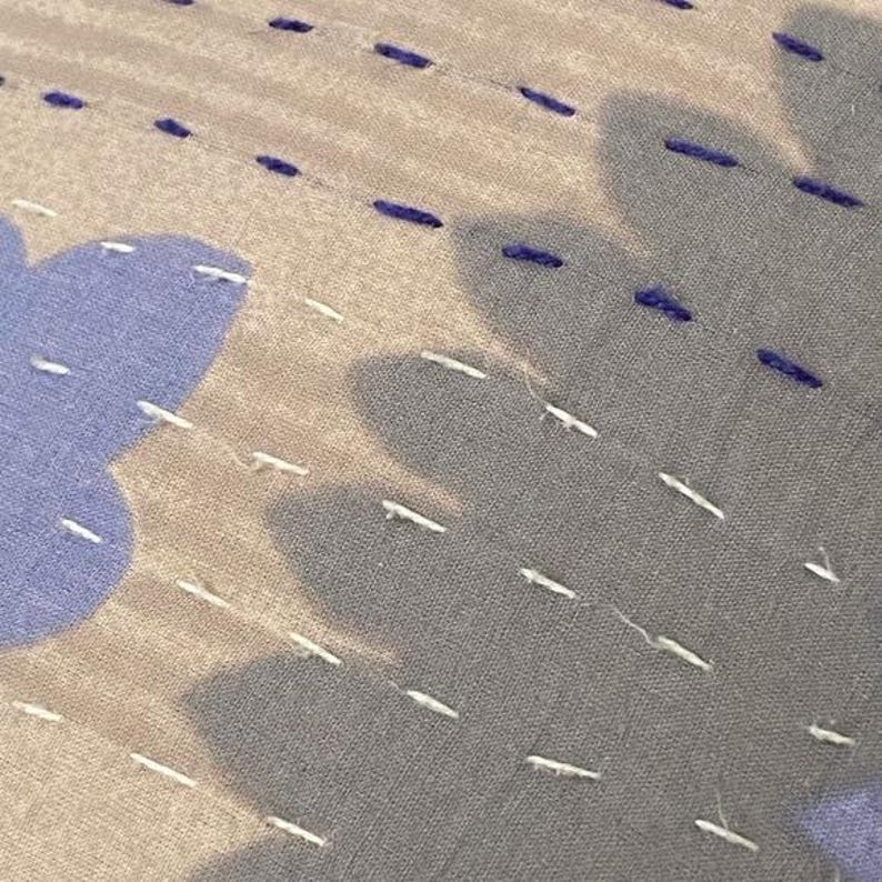 May include: Close-up of a fabric with a subtle pattern of white stitching on a light gray background. The stitching is in a diagonal pattern and creates a subtle texture.