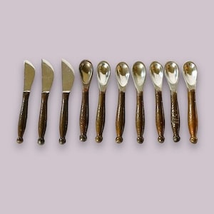 May include: Set of ten silver-toned metal spoons with brown wooden handles. The spoons are arranged in a row on a light purple background.