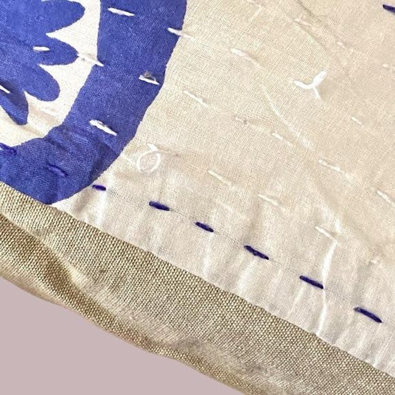 May include: Close-up of a beige pillow with a blue and white geometric pattern. The pillow is made of a soft, textured fabric and has a subtle sheen. The stitching is visible around the edges of the pillow.