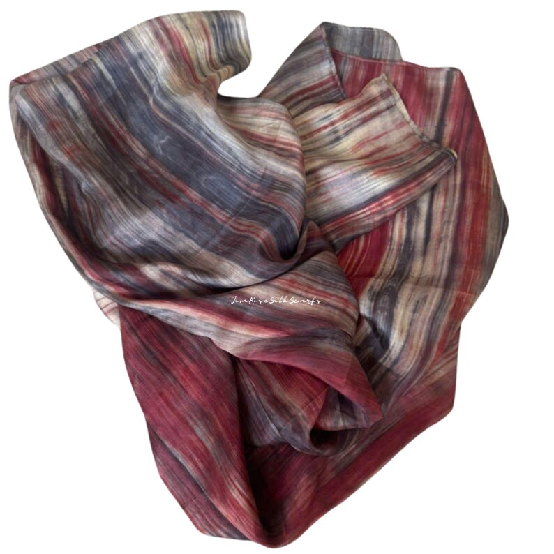 May include: A lightweight scarf featuring a vertical striped pattern in shades of deep red, charcoal grey, and cream. The fabric displays a soft, flowing texture with the text "Jim Rose Silk Scarfs" printed in white in the centre of the material.